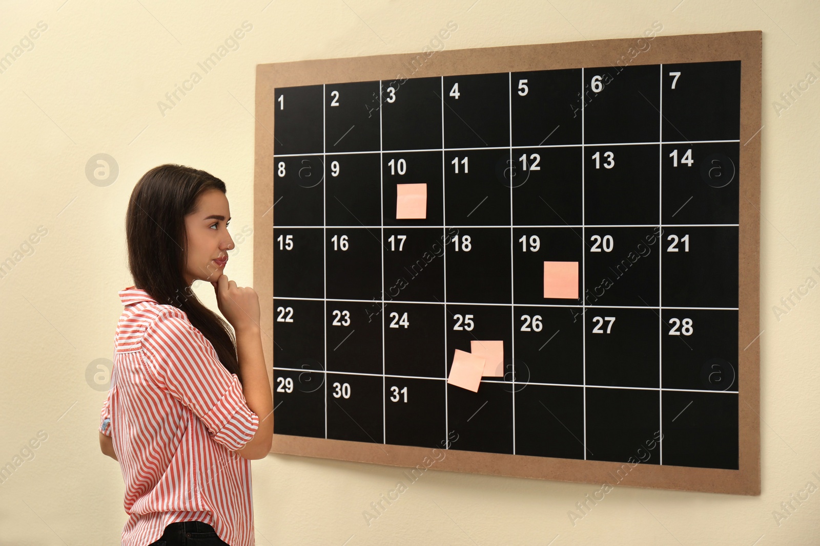 Photo of Young beautiful woman near board calendar  indoors