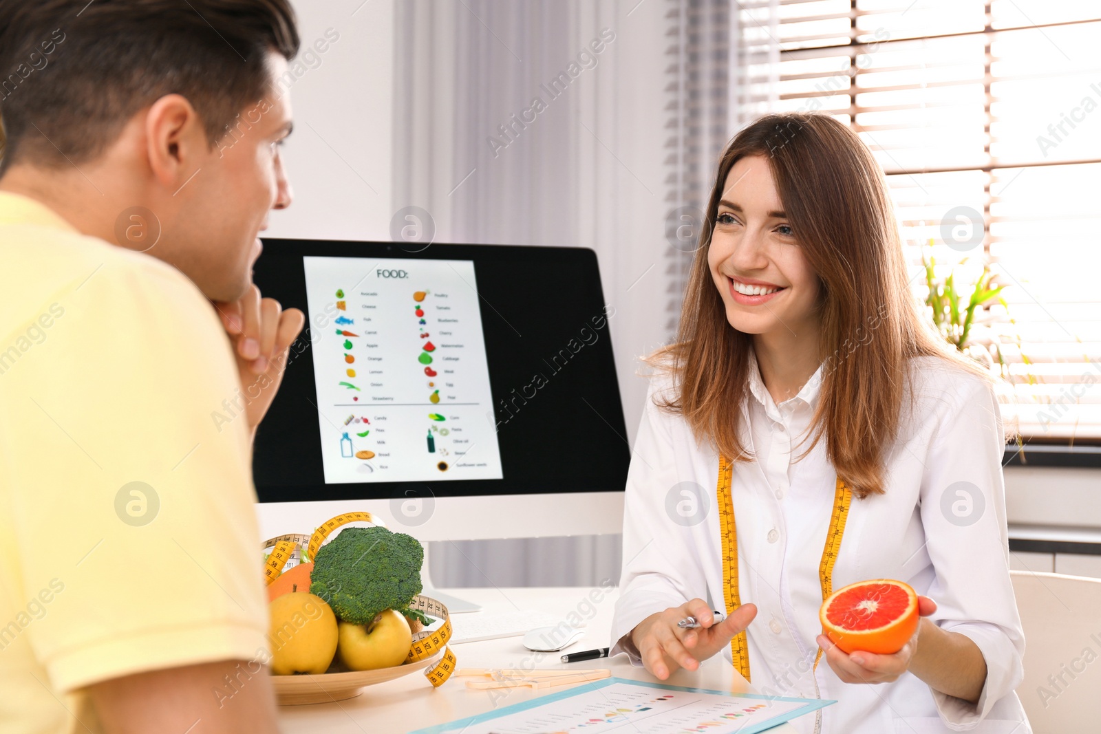 Photo of Young nutritionist consulting patient at table in clinic