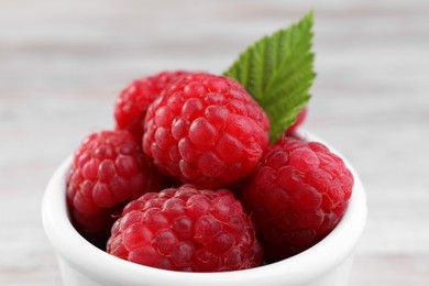 Photo of Tasty ripe raspberries and green leaf in white bowl, closeup