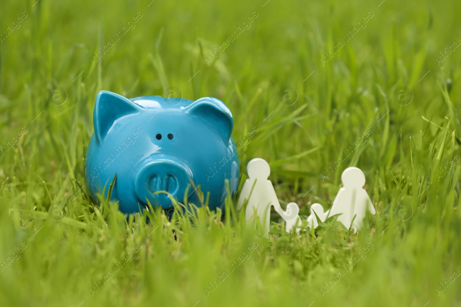 Photo of Cute piggy bank and family figure on green grass in park