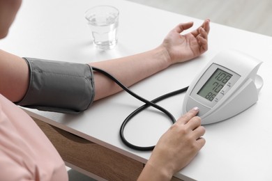 Photo of Woman measuring blood pressure with tonometer at table, closeup