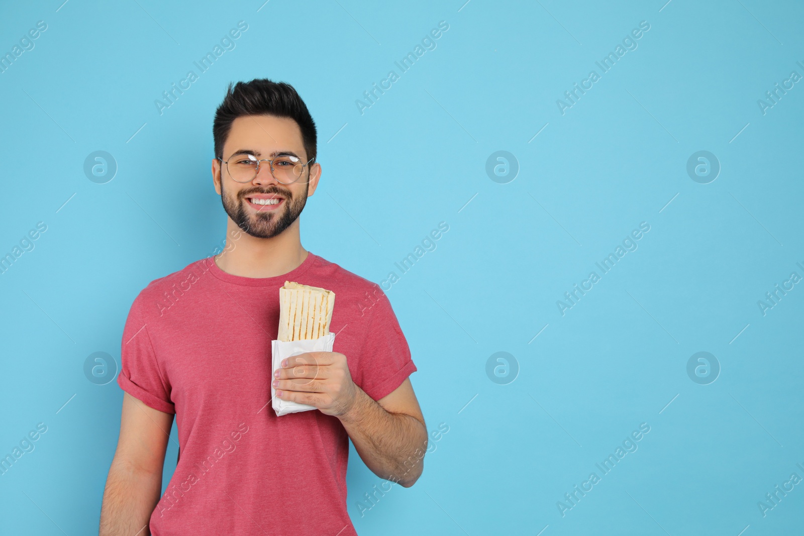 Photo of Happy young man holding tasty shawarma on turquoise background. Space for text