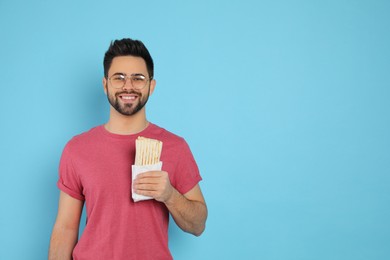 Happy young man holding tasty shawarma on turquoise background. Space for text