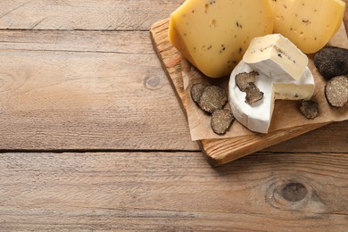 Photo of Board with delicious cheeses and fresh black truffles on wooden table, top view. Space for text