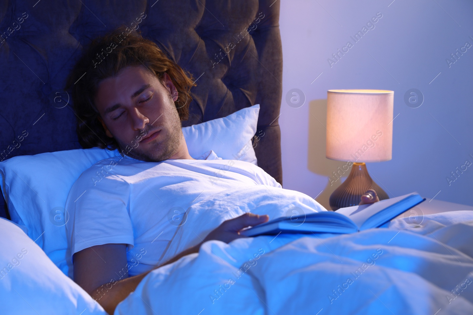 Photo of Handsome young man sleeping with book on pillow at night. Bedtime