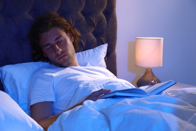Photo of Handsome young man sleeping with book on pillow at night. Bedtime