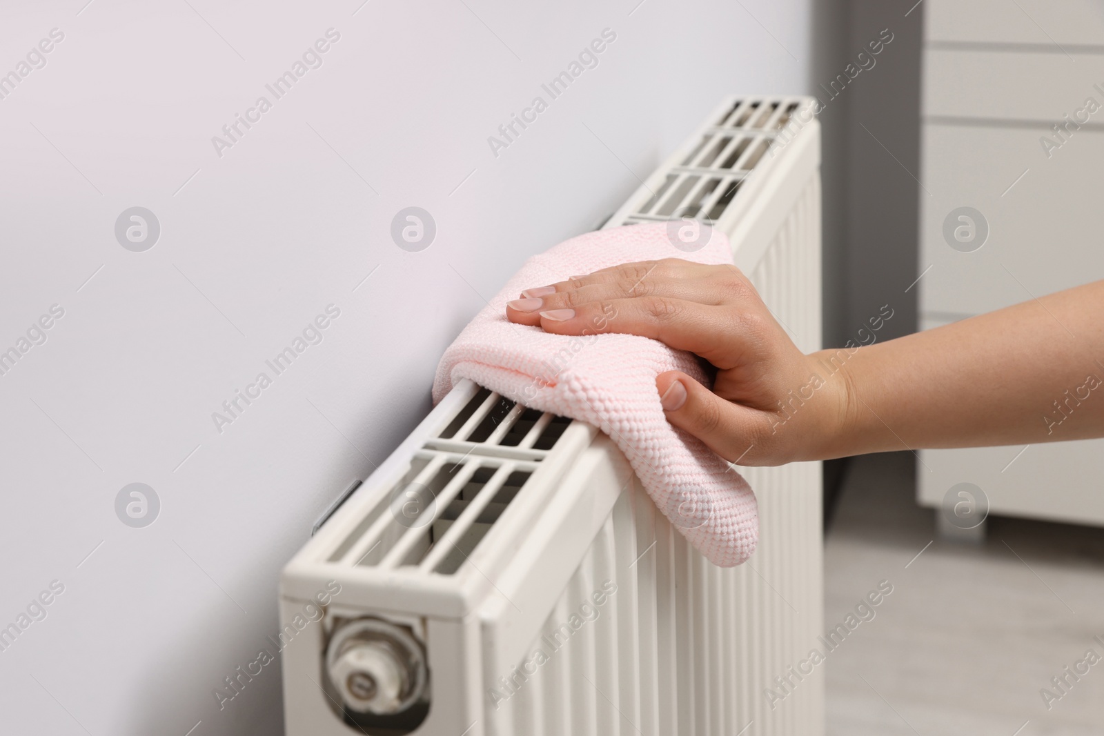 Photo of Woman cleaning radiator with rag indoors, closeup