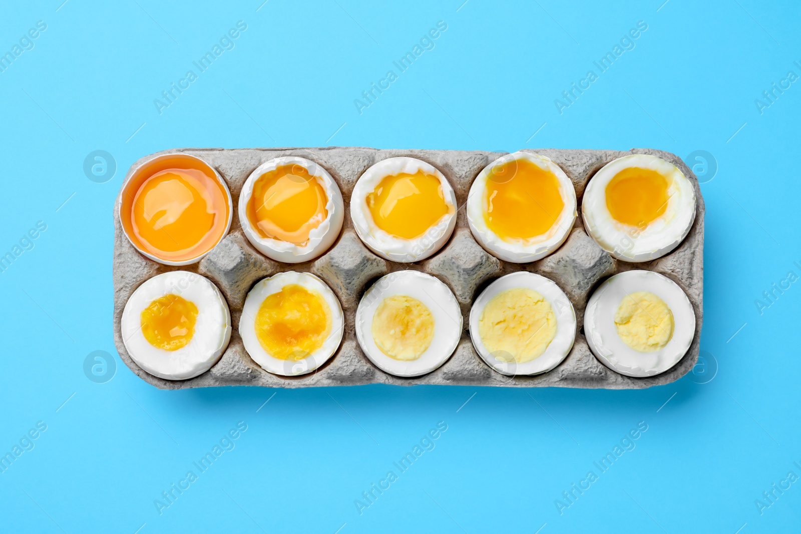 Photo of Boiled chicken eggs of different readiness stages in carton on light blue background, top view