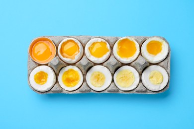 Boiled chicken eggs of different readiness stages in carton on light blue background, top view