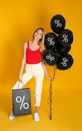 Image of Discount offer. Beautiful woman holding shopping bag and balloons with percent signs on orange background