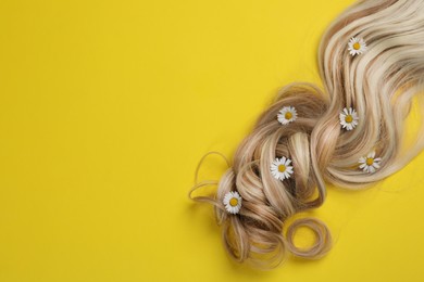 Photo of Lock of healthy blond hair with flowers on yellow background, top view. Space for text