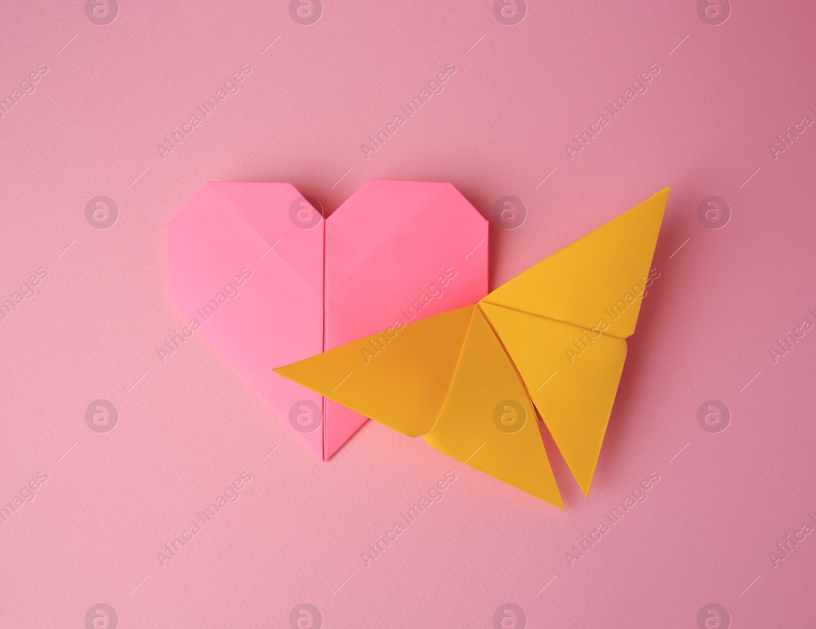 Photo of Origami art. Paper heart and butterfly on pink background, flat lay