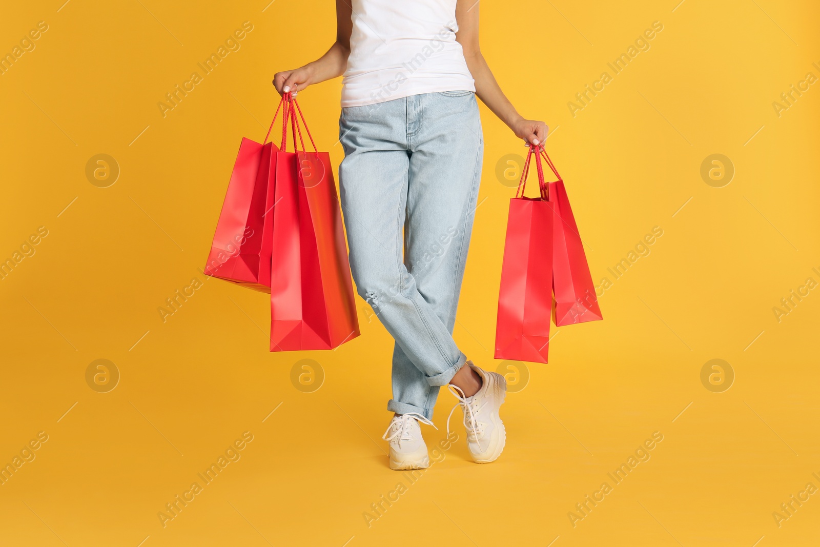 Photo of Young woman with paper shopping bags on yellow background, closeup