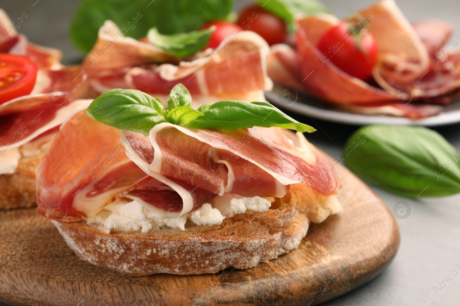 Photo of Tasty sandwich with cured ham, basil and cream cheese on grey table, closeup