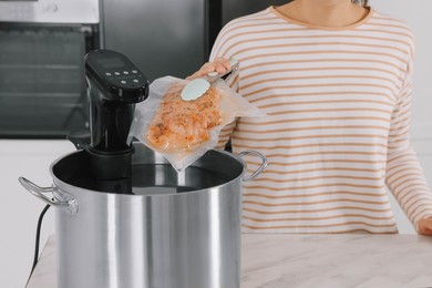 Woman putting vacuum packed meat into pot with sous vide cooker in kitchen, closeup. Thermal immersion circulator