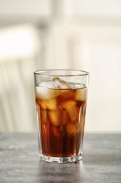 Glass of cola with ice on table against blurred background, space for text