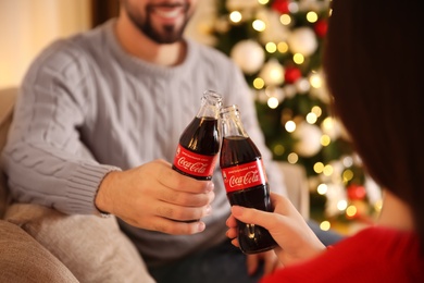 Photo of MYKOLAIV, UKRAINE - JANUARY 27, 2021: Young couple holding bottles of Coca-Cola in room decorated for Christmas, closeup