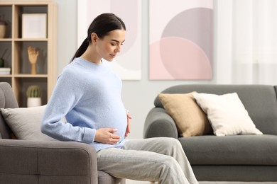 Photo of Pregnant young woman on armchair at home, space for text