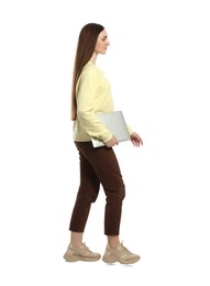 Young woman with laptop walking on white background