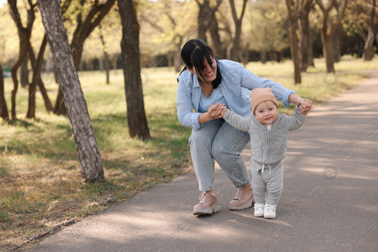 Photo of Mother supporting her baby while he learning to walk outdoors