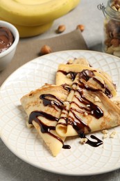 Delicious thin pancakes with chocolate spread, banana and nuts on table, closeup