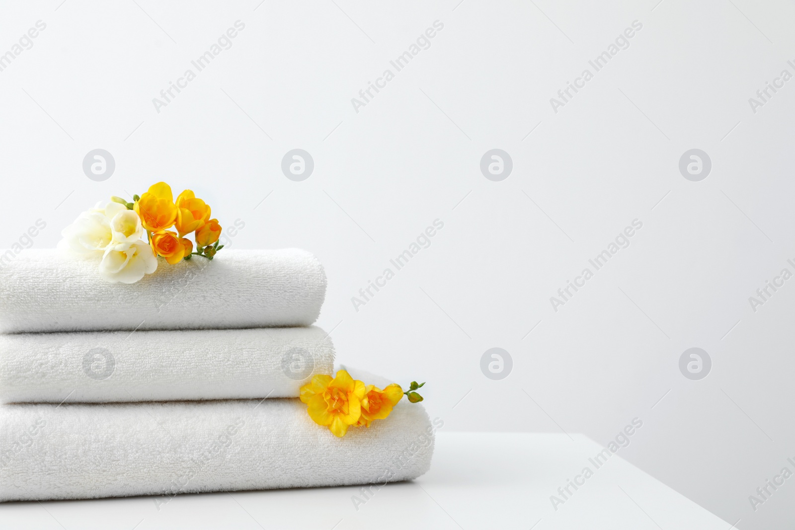 Photo of Stack of fresh towels with flowers on table against white background. Space for text