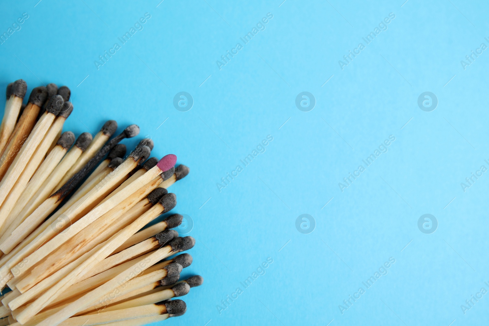 Photo of Heap of burnt matches and whole one on light blue background, flat lay. Space for text