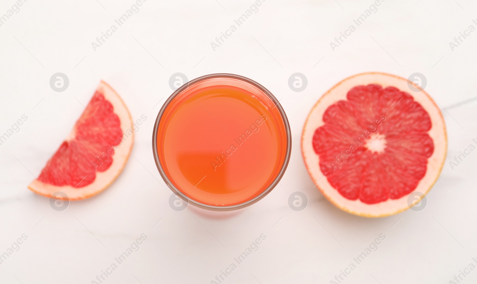 Photo of Tasty grapefruit juice in glass and slices of fresh fruit on white table, top view