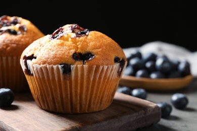 Wooden board with blueberry muffins on grey table against black background, closeup view. Space for text