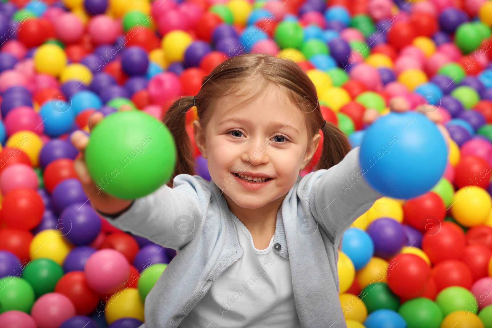 Photo of Happy little girl holding colorful balls in ball pit