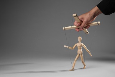 Photo of Man pulling strings of puppet on gray background, closeup. Space for text