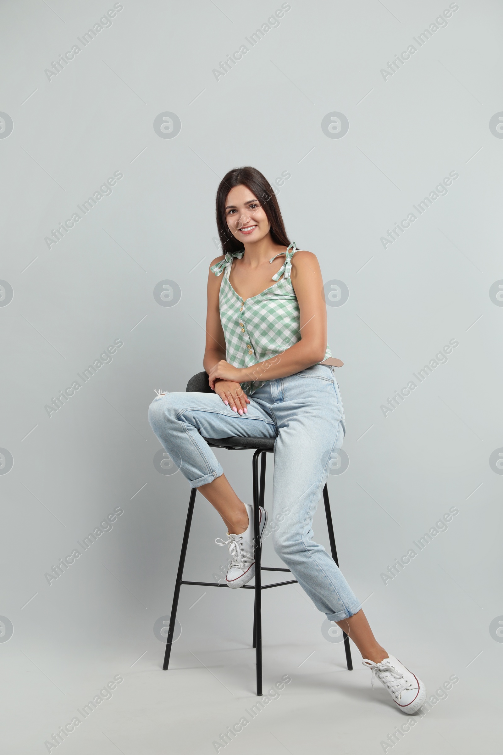 Photo of Beautiful young woman sitting on stool against light grey background