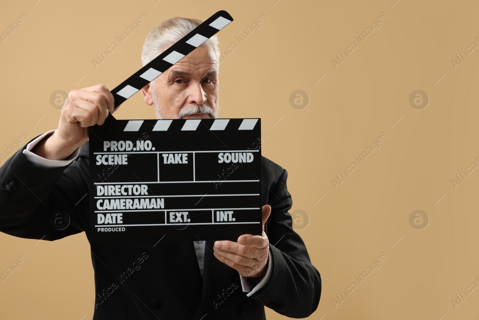 Photo of Senior actor holding clapperboard on beige background, space for text. Film industry