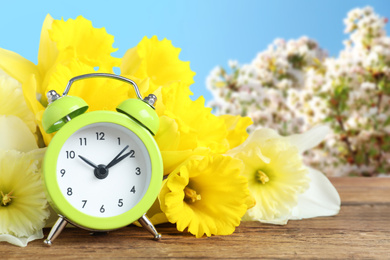 Alarm clock and flowers on wooden table against blurred background. Spring time