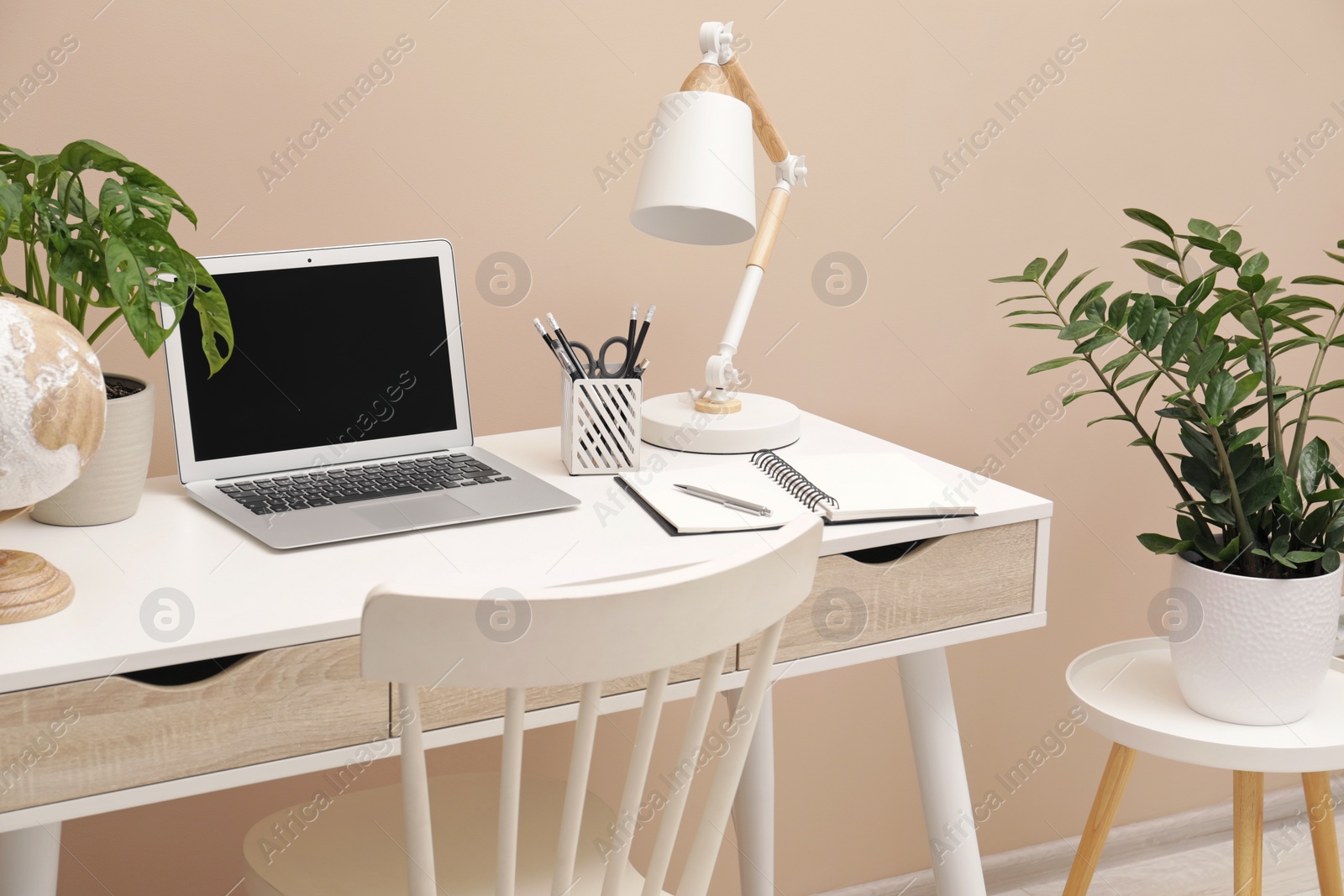 Photo of Cozy workplace with modern laptop on desk and comfortable chair at home