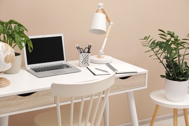 Photo of Cozy workplace with modern laptop on desk and comfortable chair at home