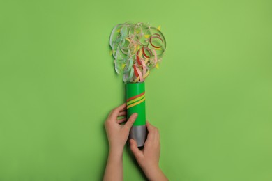 Photo of Woman holding party popper with serpentine and confetti on green background, top view