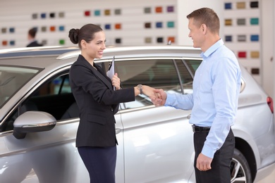 Photo of Young saleswoman working with client in car dealership