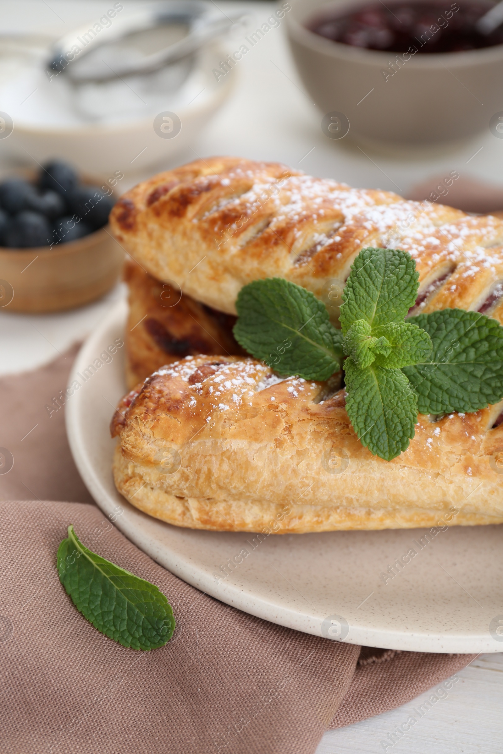 Photo of Fresh tasty puff pastry with sugar powder and mint on white table, closeup