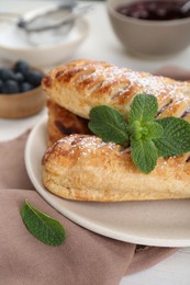 Photo of Fresh tasty puff pastry with sugar powder and mint on white table, closeup