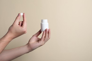 Man holding pill and bottle on beige background, closeup. Space for text