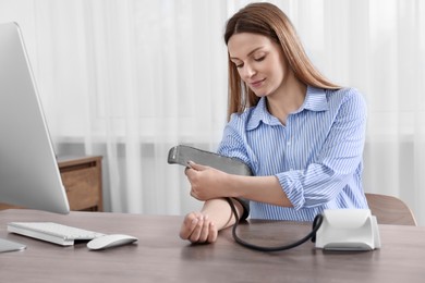 Photo of Woman measuring blood pressure at wooden table in room, space for text