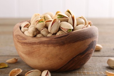 Tasty pistachios in bowl on wooden table, closeup