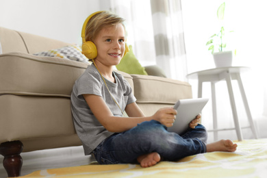 Photo of Cute little boy with headphones and tablet listening to audiobook at home