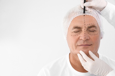 Doctor marking senior man face before cosmetic surgery on white background. Space for text