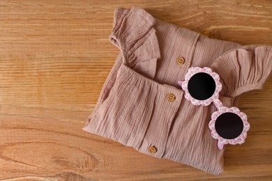 Photo of Stylish child clothes and sunglasses on wooden background, flat lay. Space for text