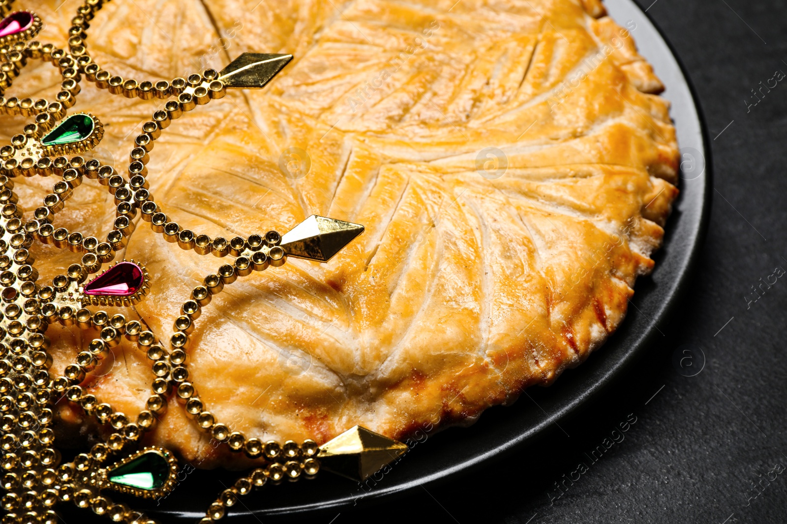 Photo of Traditional galette des rois with crown on black table, closeup