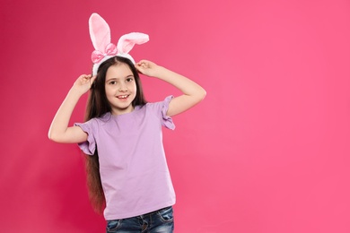 Portrait of little girl in Easter bunny ears headband on color background, space for text