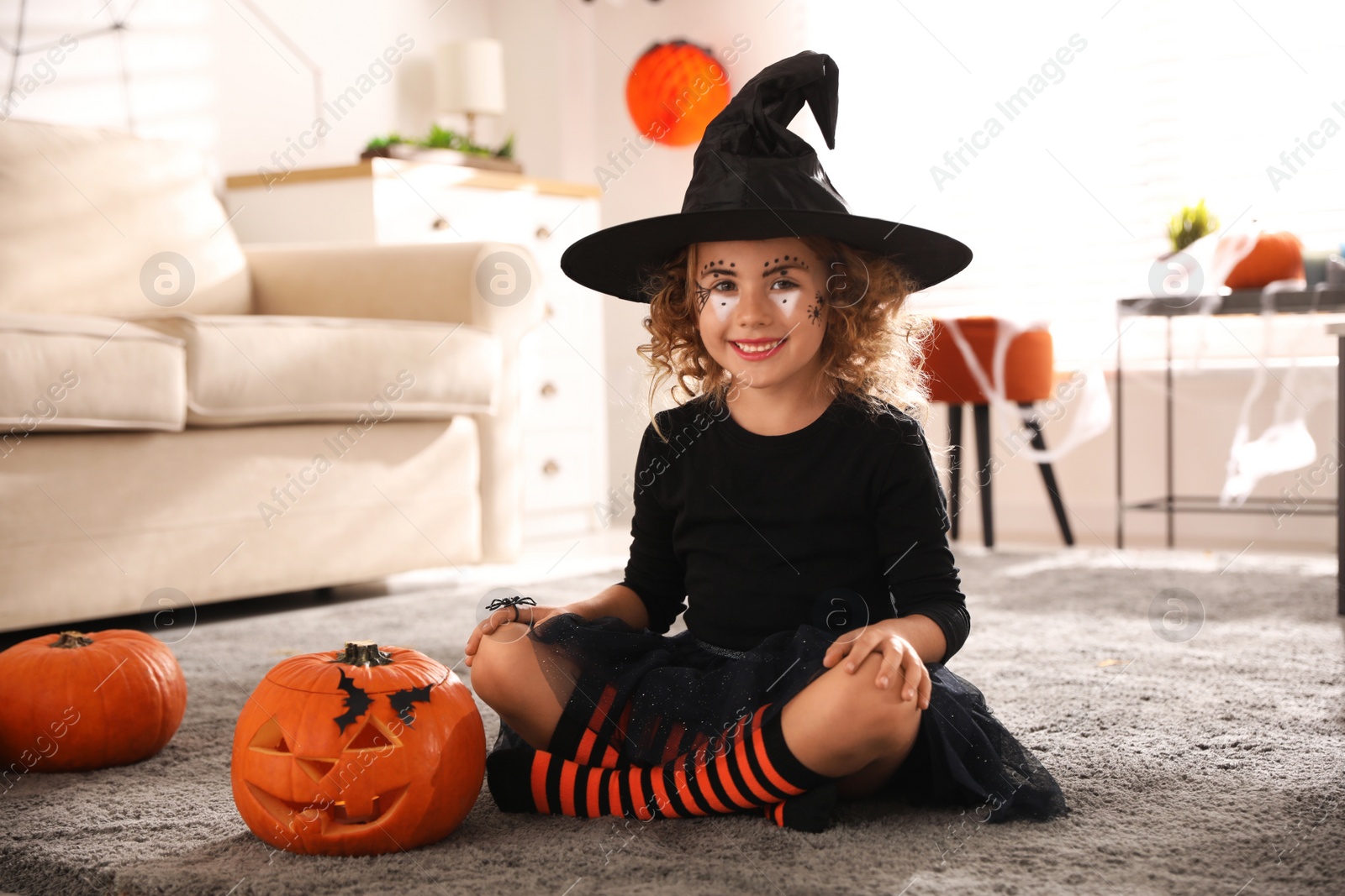 Photo of Cute little girl with pumpkin wearing Halloween costume at home
