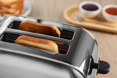 Photo of Closeup view of toaster with roasted bread on wooden table